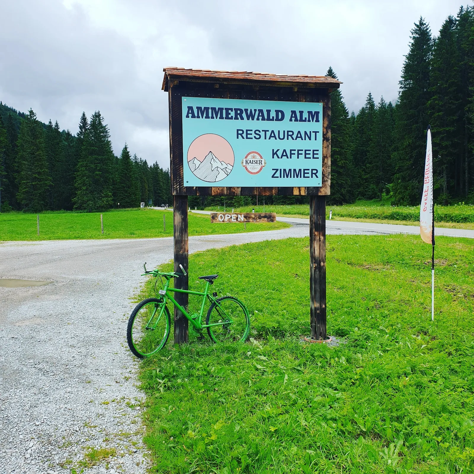 Großes gefertigtes Schild der Ammerwald Alm vor Wald und Berglandschaft